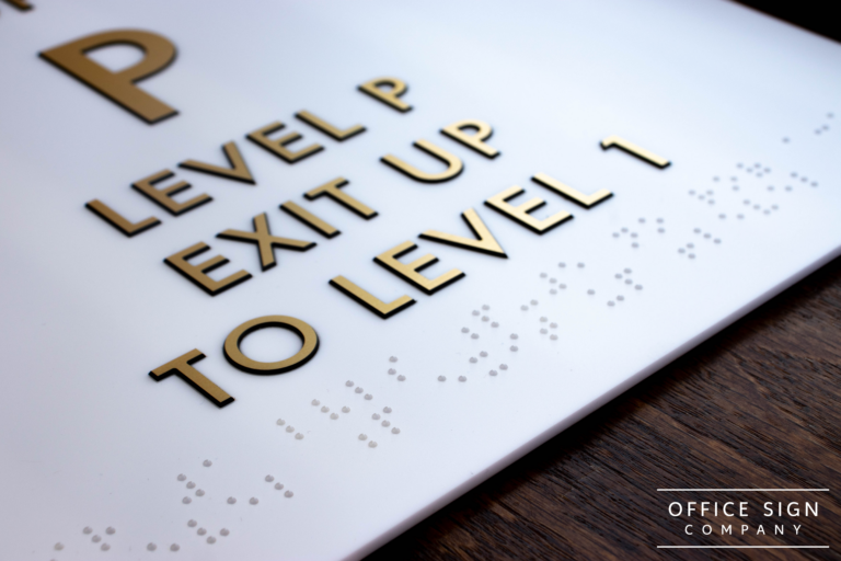 White plastic sign with the text: "P, Level P, Exit Up, To Level 1" with braille text below